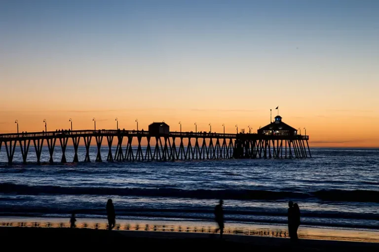 A pier, beach, and ocean at sunset.